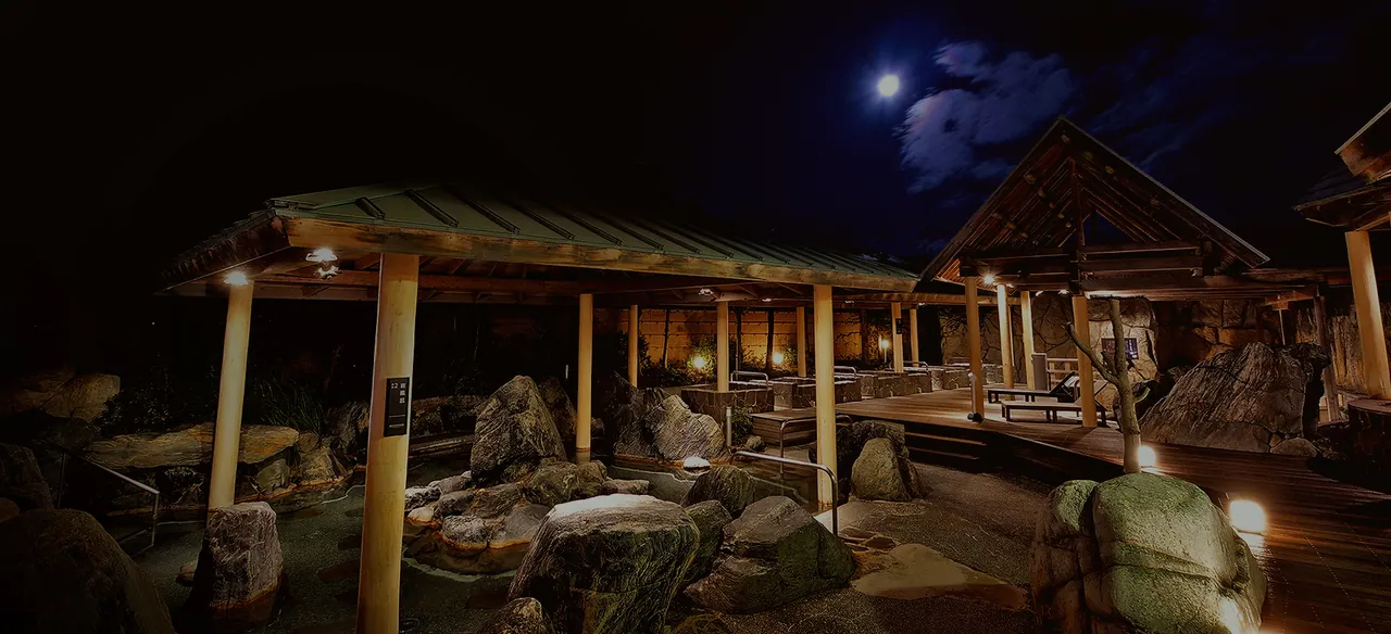 The open-air bath at night, lantern light reflecting on the water